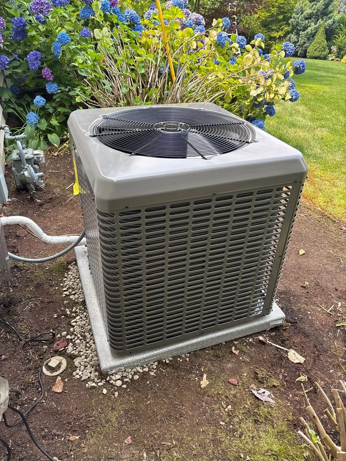 A newly installed air conditioner condenser on a level pad set in gravel