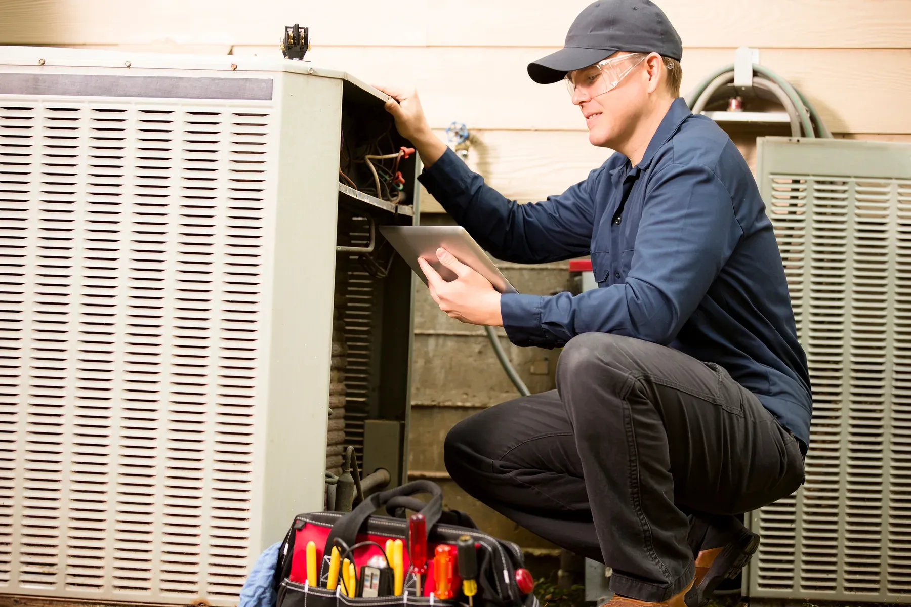 A Comfy technician reading refrigerant pressures on a manifold gauge set at an outdoor air conditioning unit